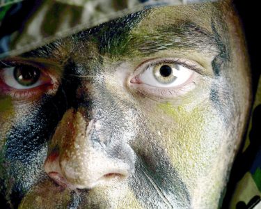 young soldier face with jungle camouflage paint